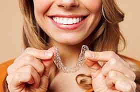 Smiling woman holding Invisalign aligner close to her mouth