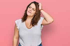 Woman standing against pink background, scratching her head